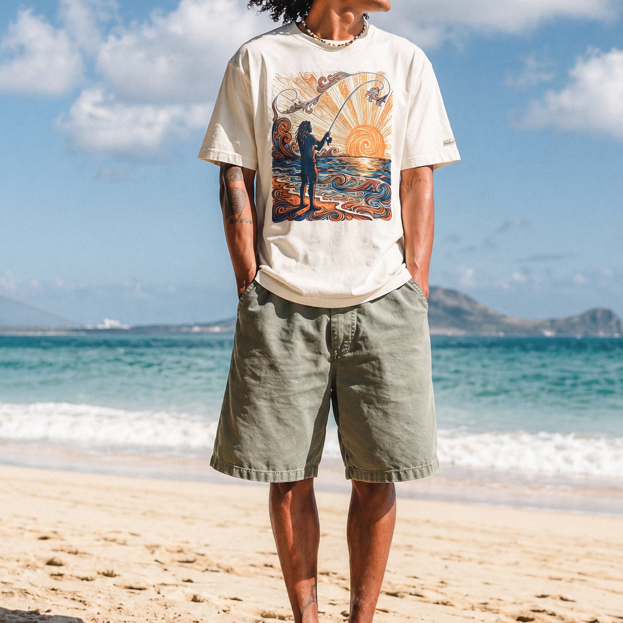 a man standing on the beach wearing a pearl colored shirt with a colorful graphic of a person fishing