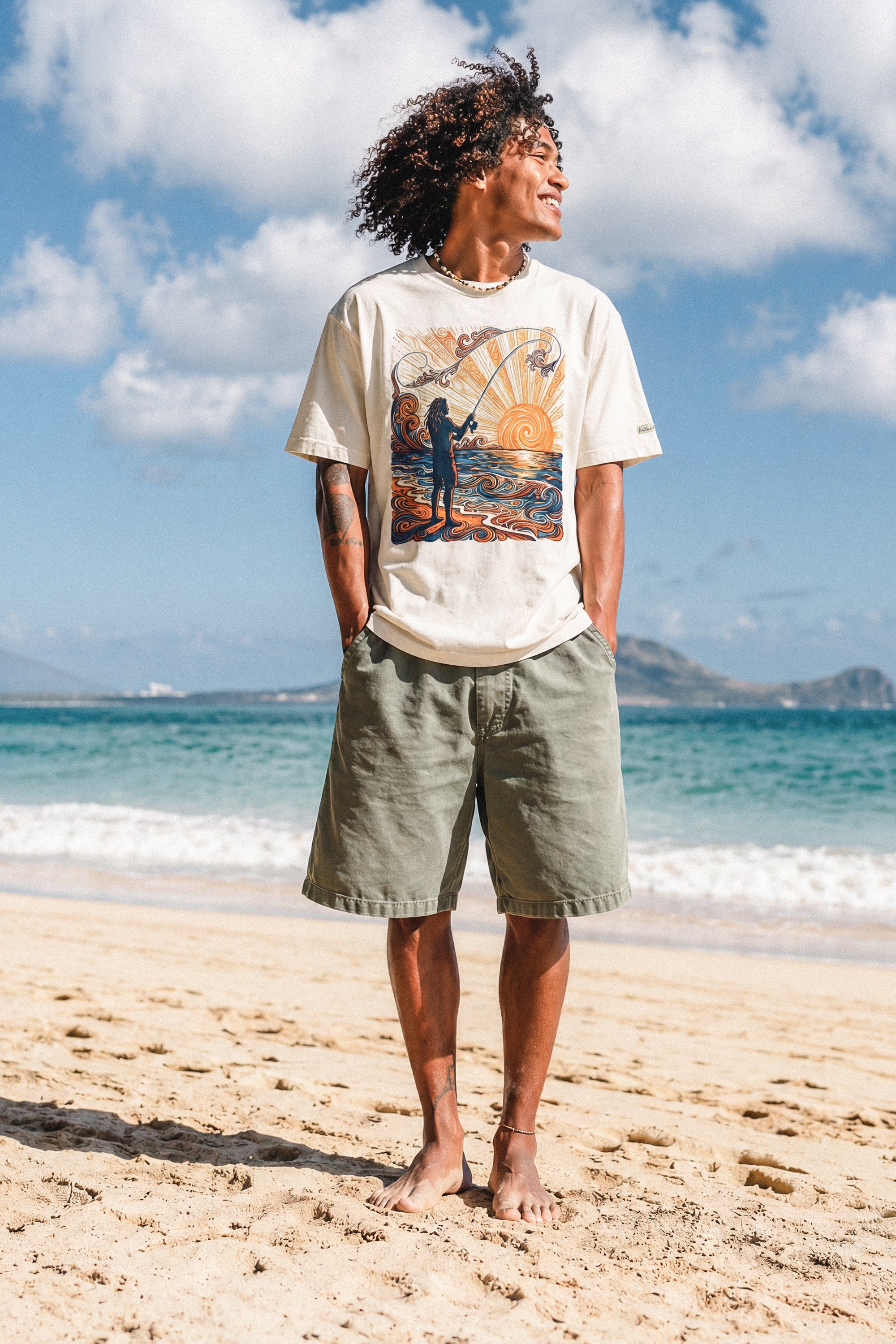 a man standing on the beach wearing a pearl colored shirt with a colorful graphic of a person fishing