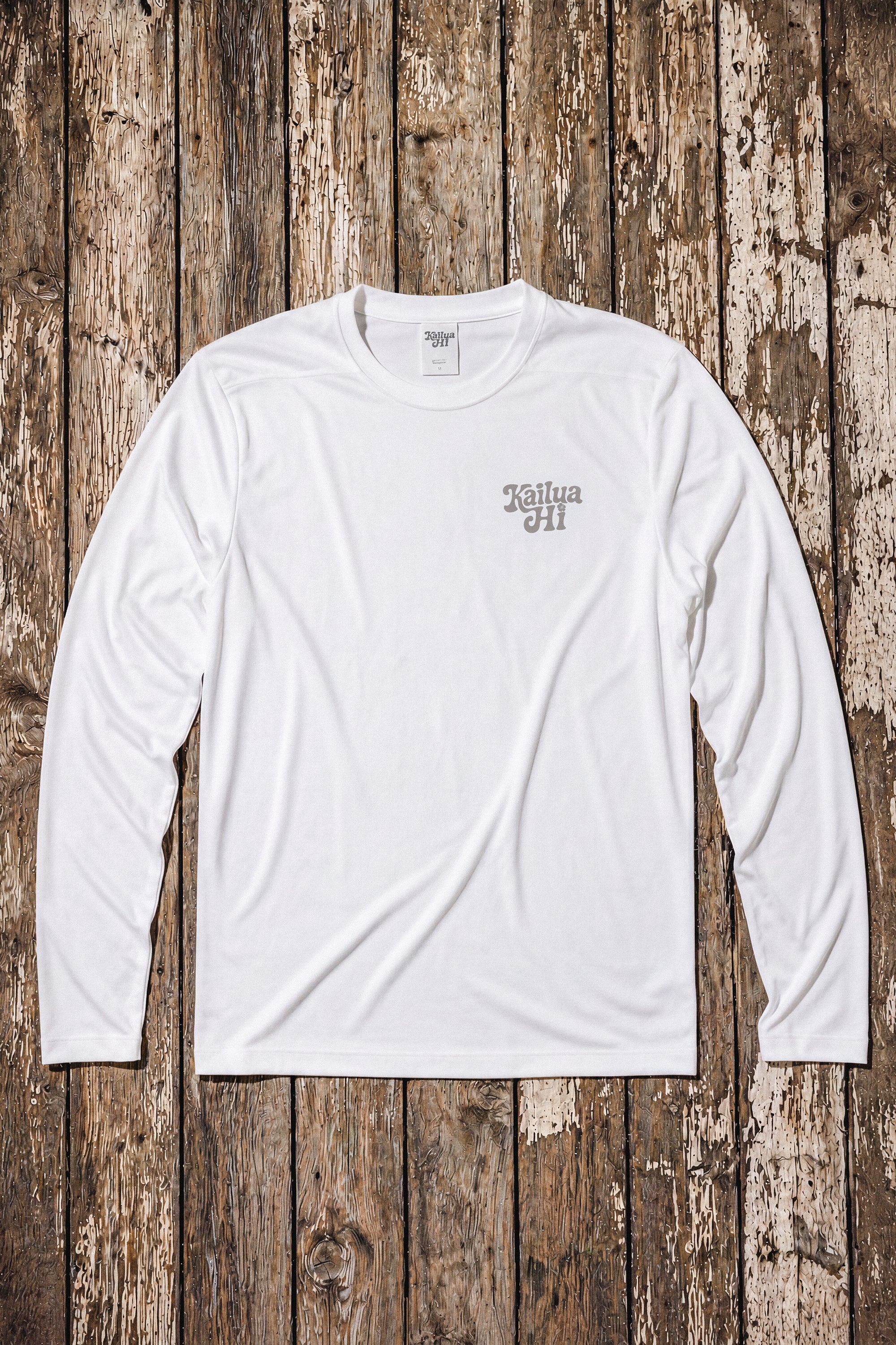 White long-sleeve shirt with a Kailua Hi logo on the left chest on a wooden surface