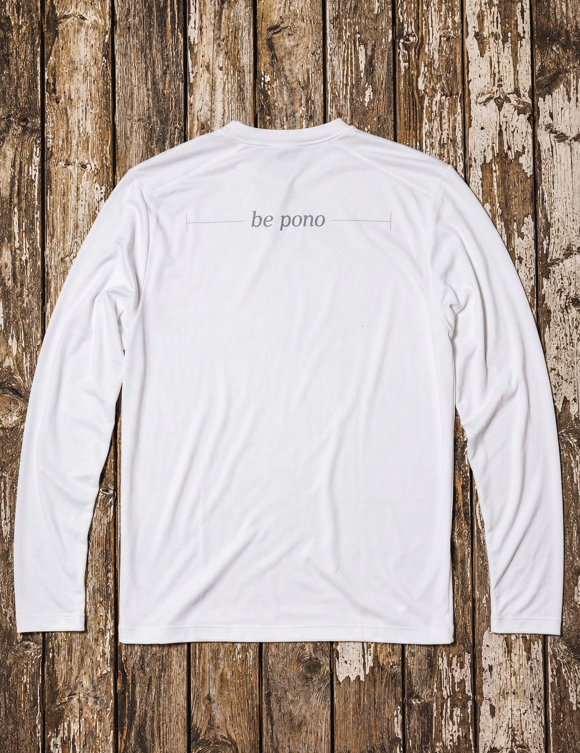 White long-sleeve shirt with 'be pono' text on a wooden background