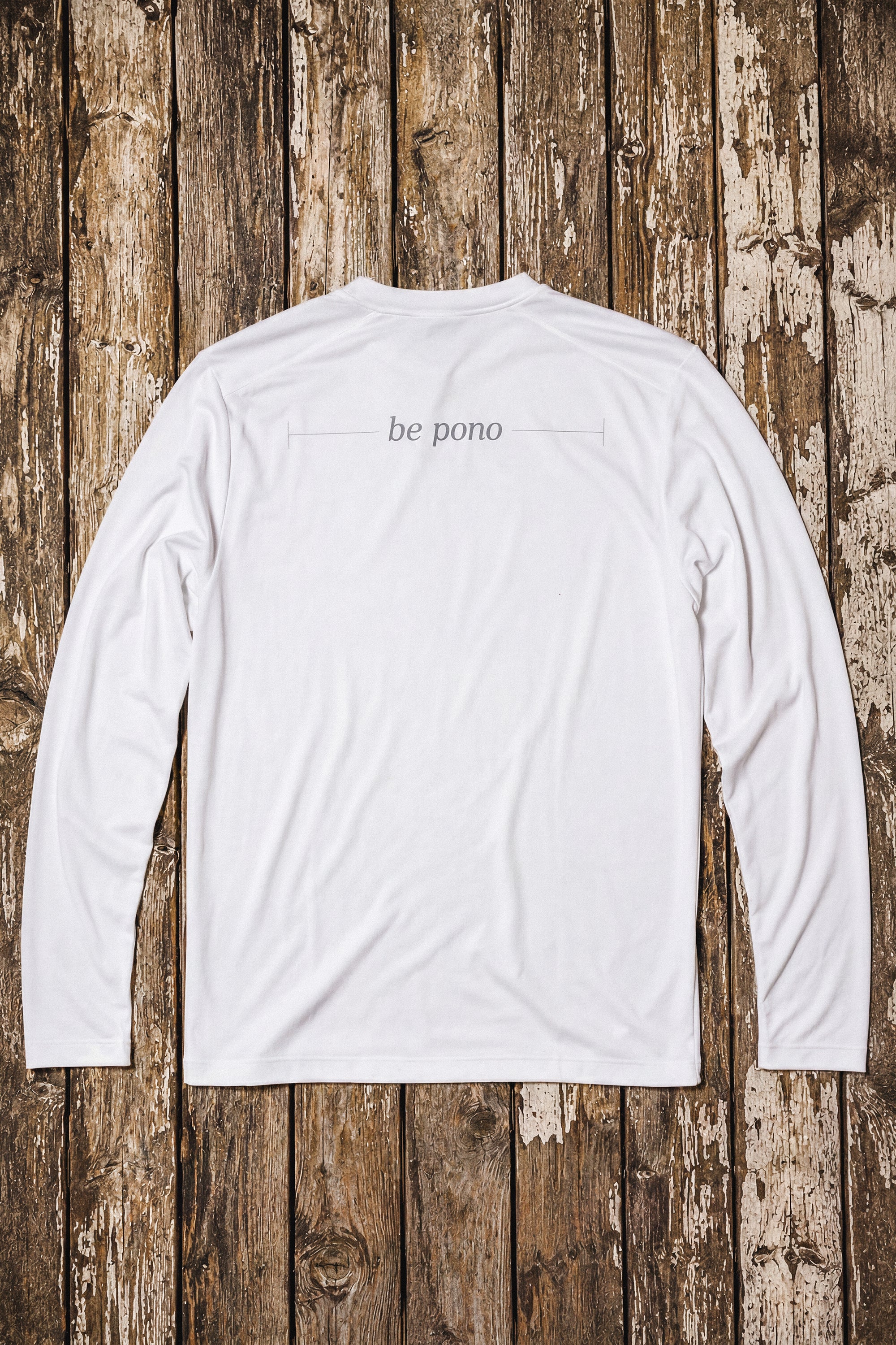 White long-sleeve shirt with 'be pono' text on a wooden background