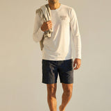 man wearing white long sleeve shirt with gray kailua hi logo on chest and black shorts with a towel over his shoulder