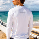 A man wearing a white long-sleeve shirt with 'be pono' graphic on the beach.