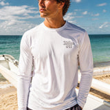 Man wearing a white long-sleeve shirt with a Kailua Hi logo on the left chest on a beach