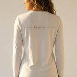 woman wearing a white long-sleeve shirt with grey 'be pono' text on the back against a plain background