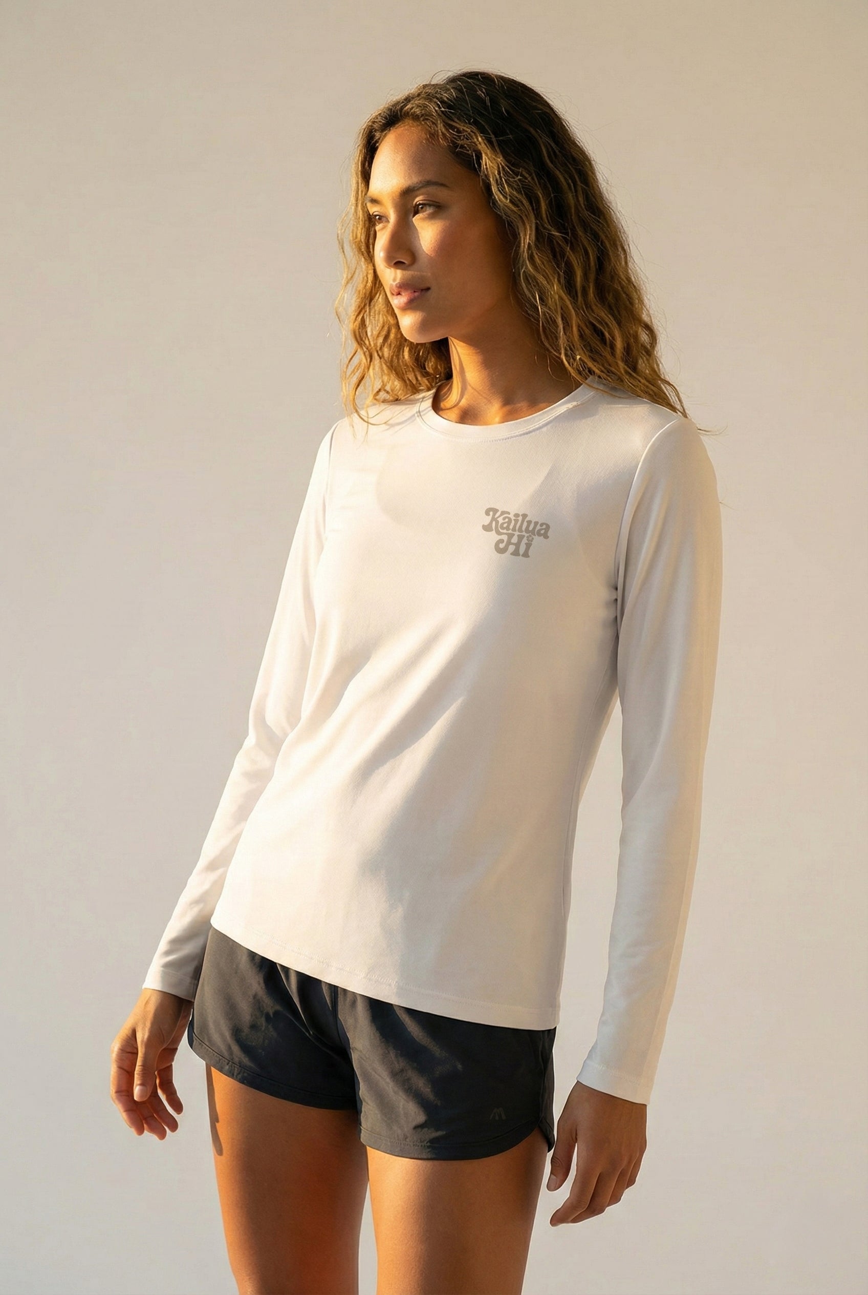 Woman wearing a white long-sleeve shirt with a Kailua Hi logo on a plain background