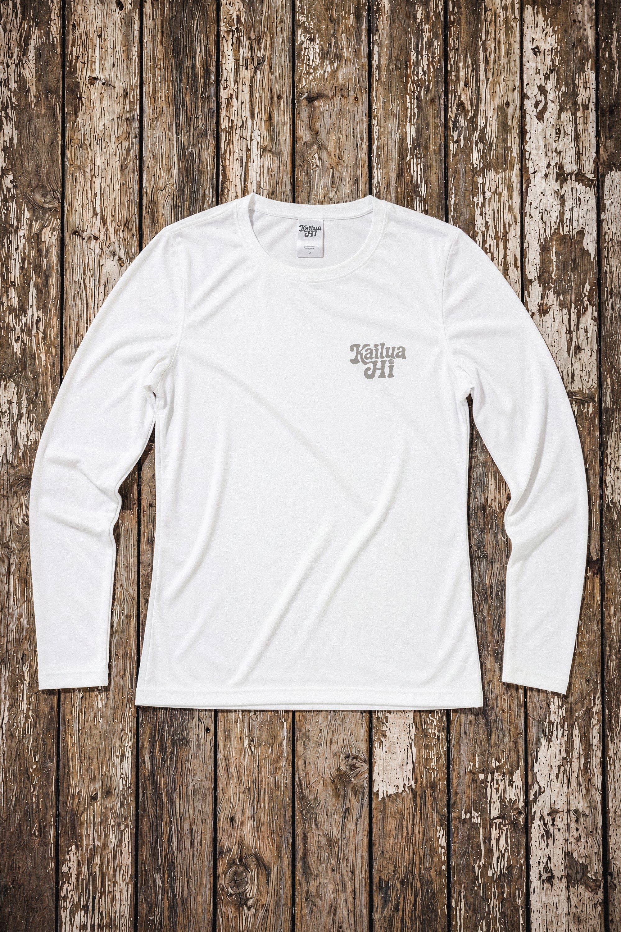 White long-sleeve shirt with a Kailua Hi Logo on the left chest on a wooden floor
