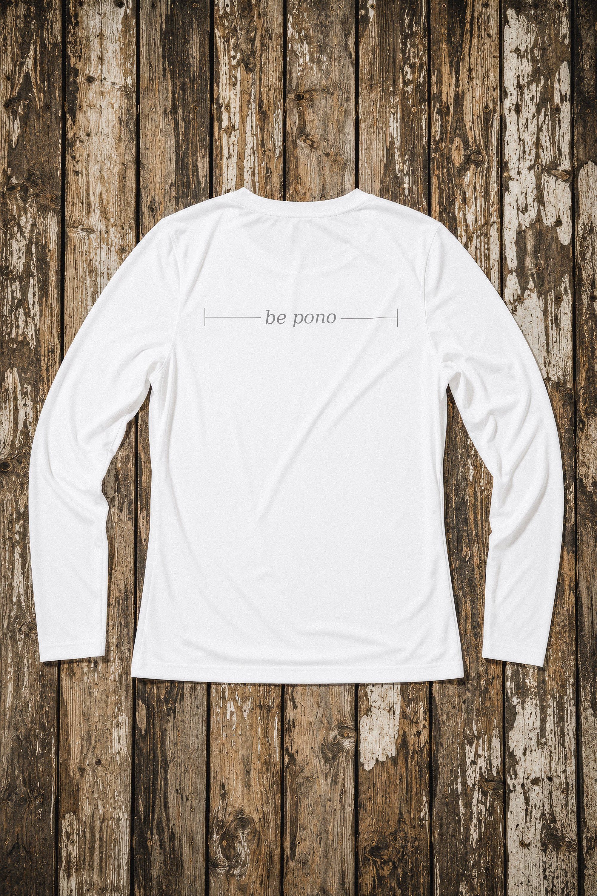 White long-sleeve shirt with 'be pono' text on a wooden background