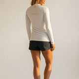 Woman wearing a white long-sleeve rash guard with grey "be pono" text on the back and black shorts on a plain background