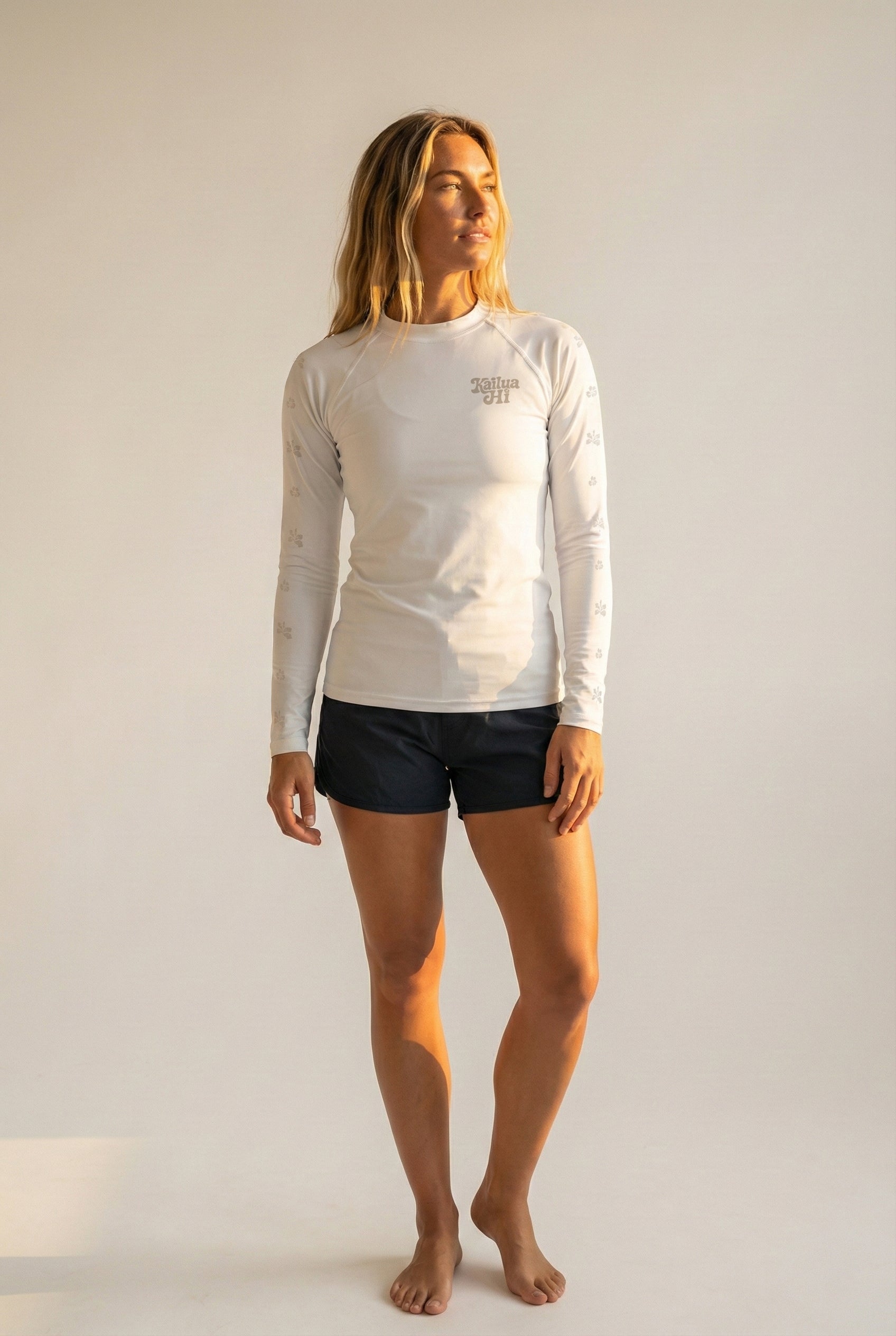 Woman wearing a white long-sleeve shirt and black shorts on a plain background