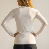 Person wearing a white long-sleeve athletic shirt with grey 'be pono' text on the back, standing against a plain background.