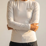 woman wearing a white long-sleeve shirt with a Kailua Hi logo and black shorts against a plain background