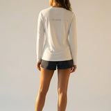 Woman wearing a white long-sleeve shirt with grey "be pono" text on a plain background