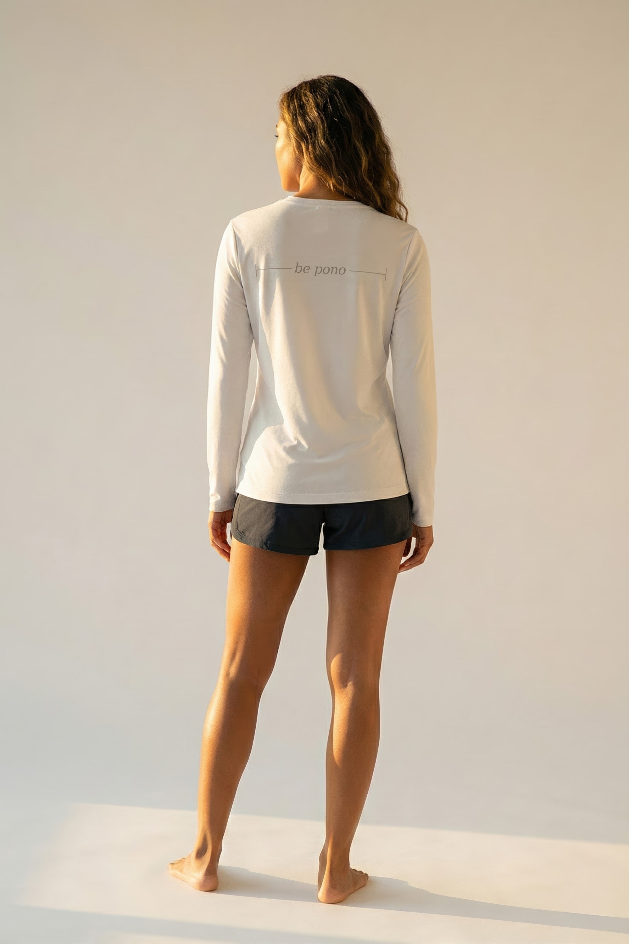 Woman wearing a white long-sleeve shirt with grey "be pono" text on a plain background