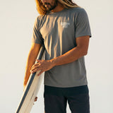 man holding a surfboard wearing a grey short sleeve tee with a kailua hi logo on front