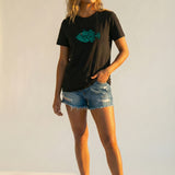 Woman wearing a black t-shirt with a blue fish graphic and denim shorts on a white background