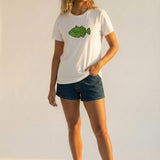 Woman wearing a white t-shirt with a green fish graphic and dark shorts on a light background