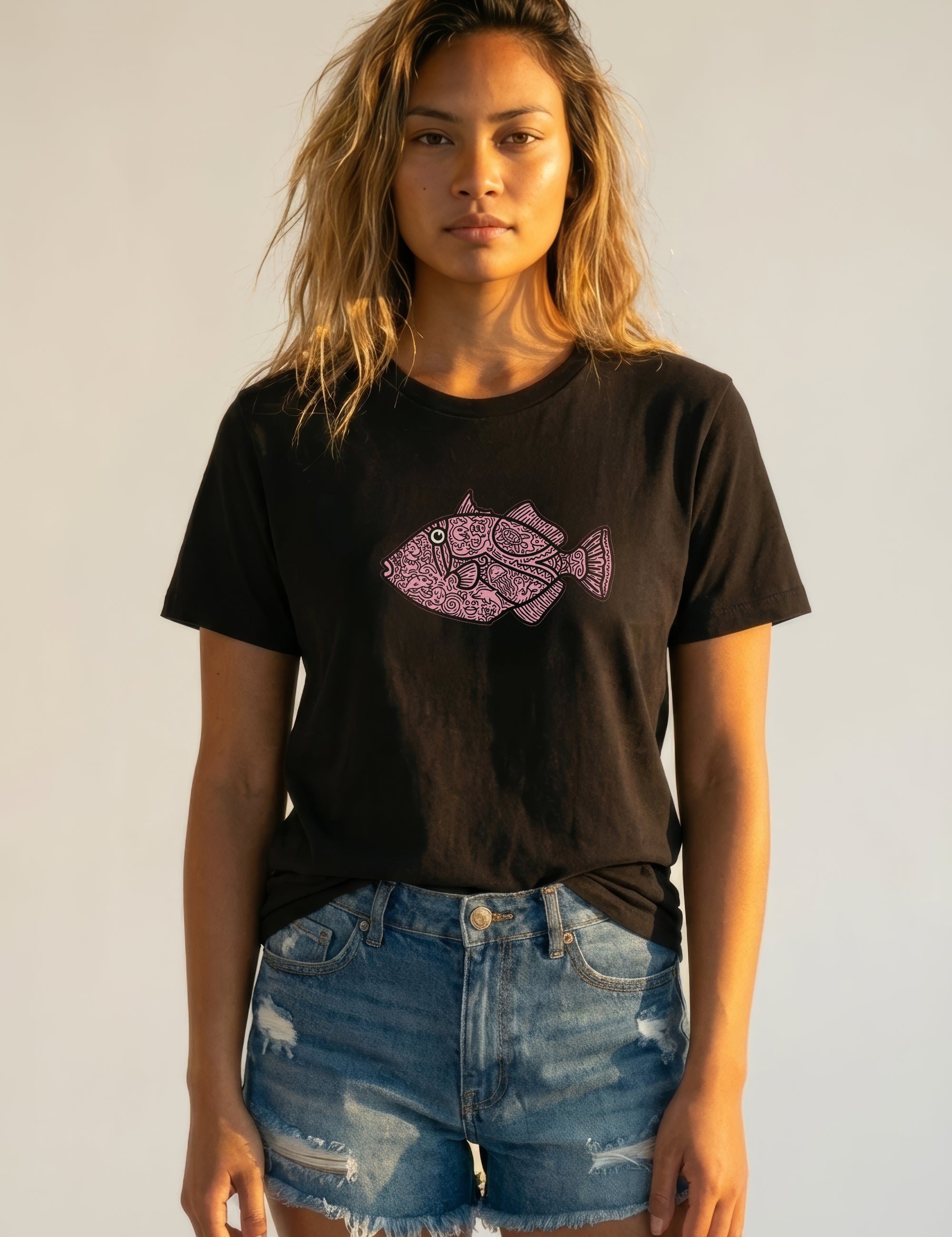 Woman wearing a black t-shirt with a pink fish design and denim shorts against a plain background