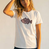 Woman wearing a white t-shirt with a pink fish graphic on a plain background