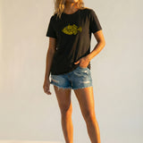 Woman wearing a black t-shirt with a yellow fish graphic and denim shorts on a white background