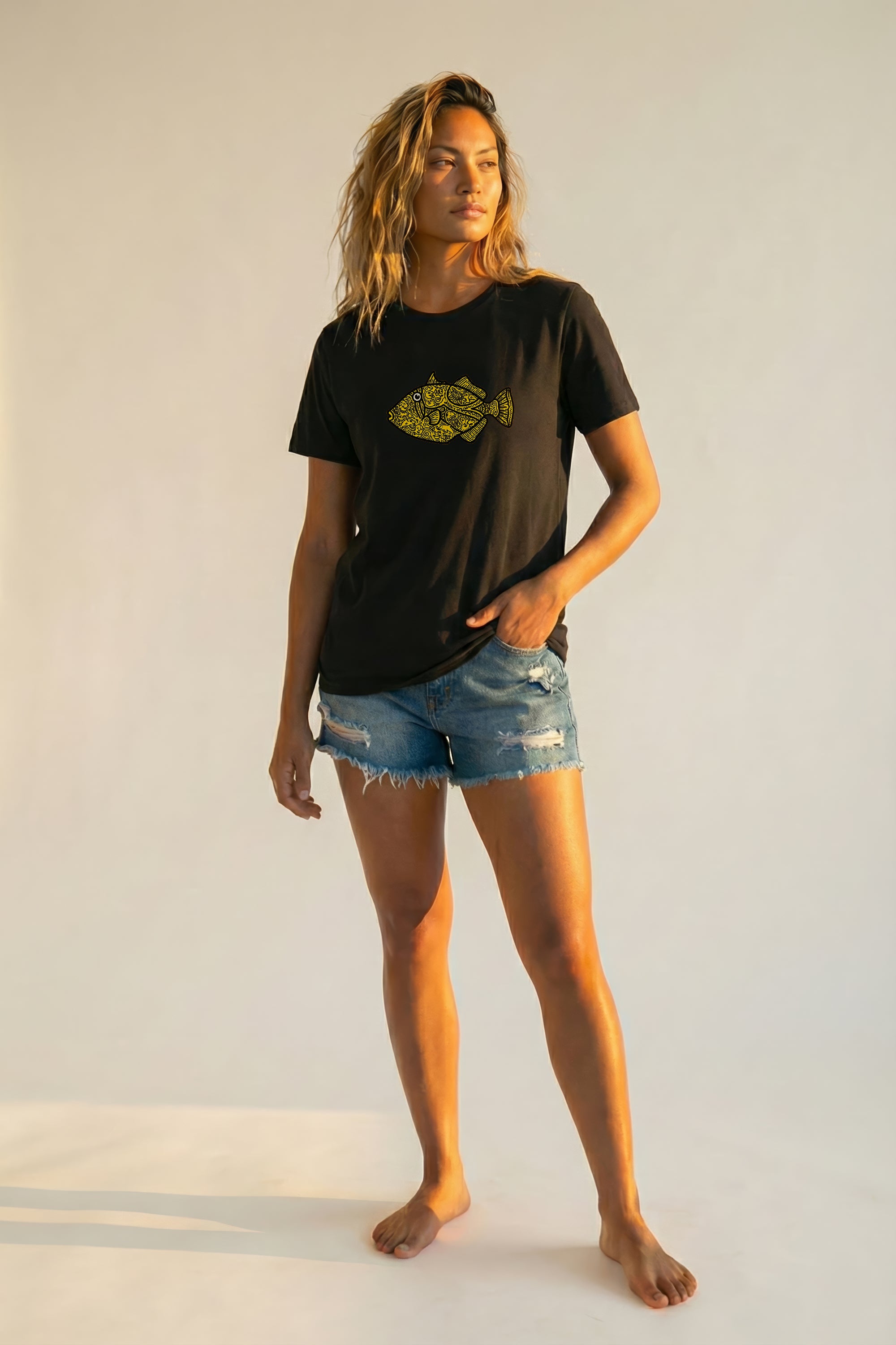 Woman wearing a black t-shirt with a yellow fish graphic and denim shorts on a white background