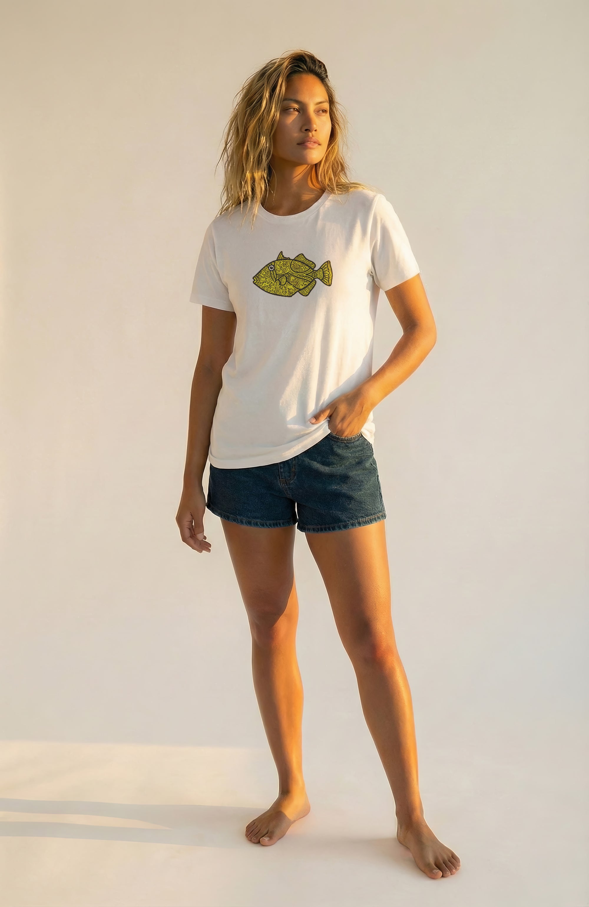 Woman wearing a white t-shirt with a yellow fish graphic and dark shorts on a plain background