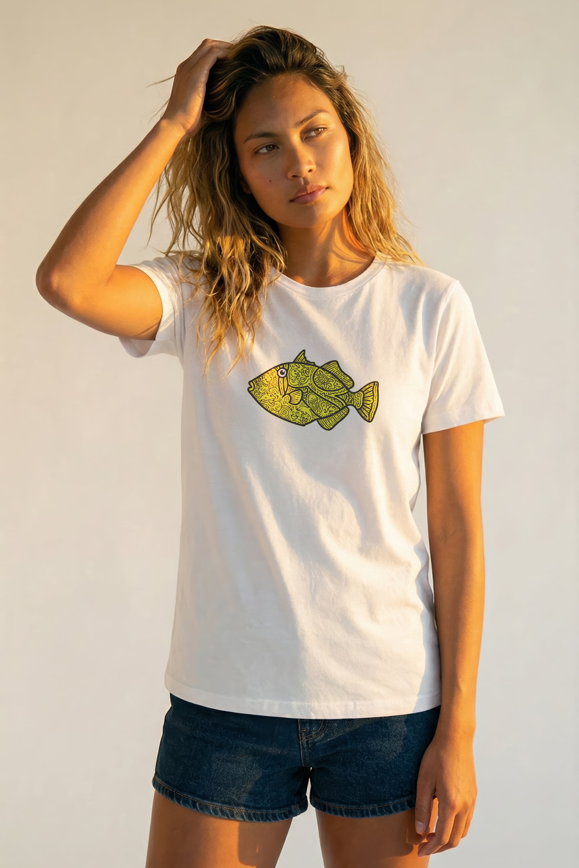 Woman wearing a white t-shirt with a yellow fish graphic on a plain background