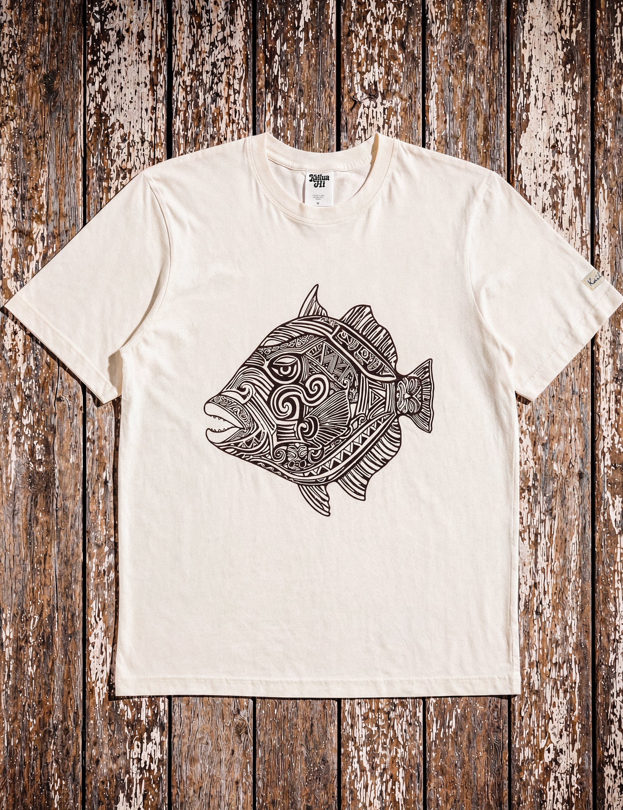 a pearl colored t-shirt with a fish graphic laying on a wood floor