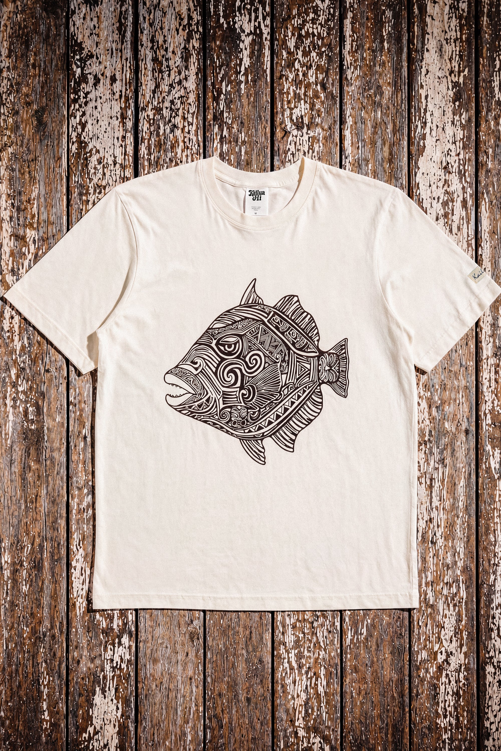 a pearl colored t-shirt with a fish graphic laying on a wood floor