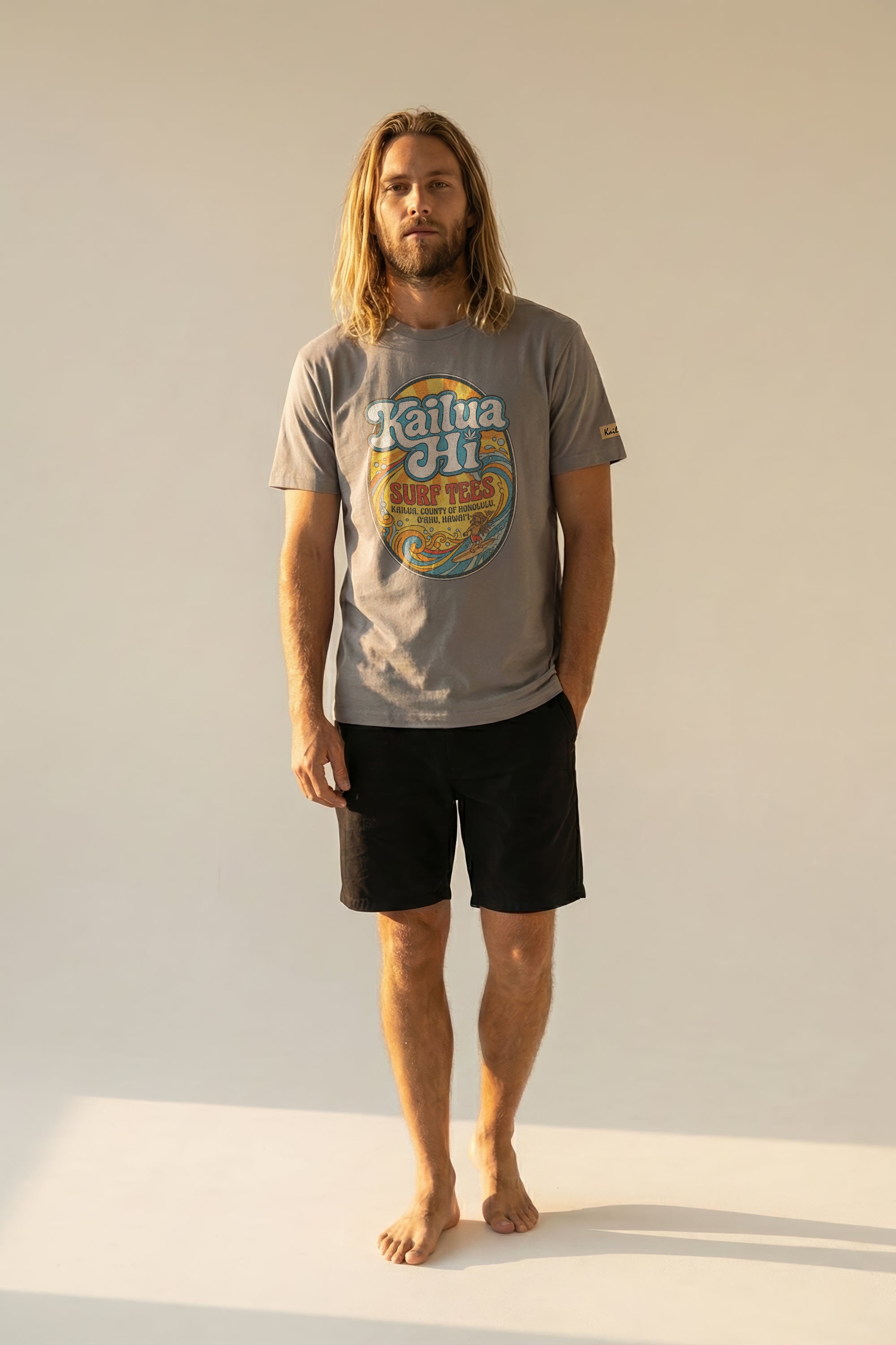 Man wearing a gray t-shirt with kailua hi logo design and black shorts on a plain background