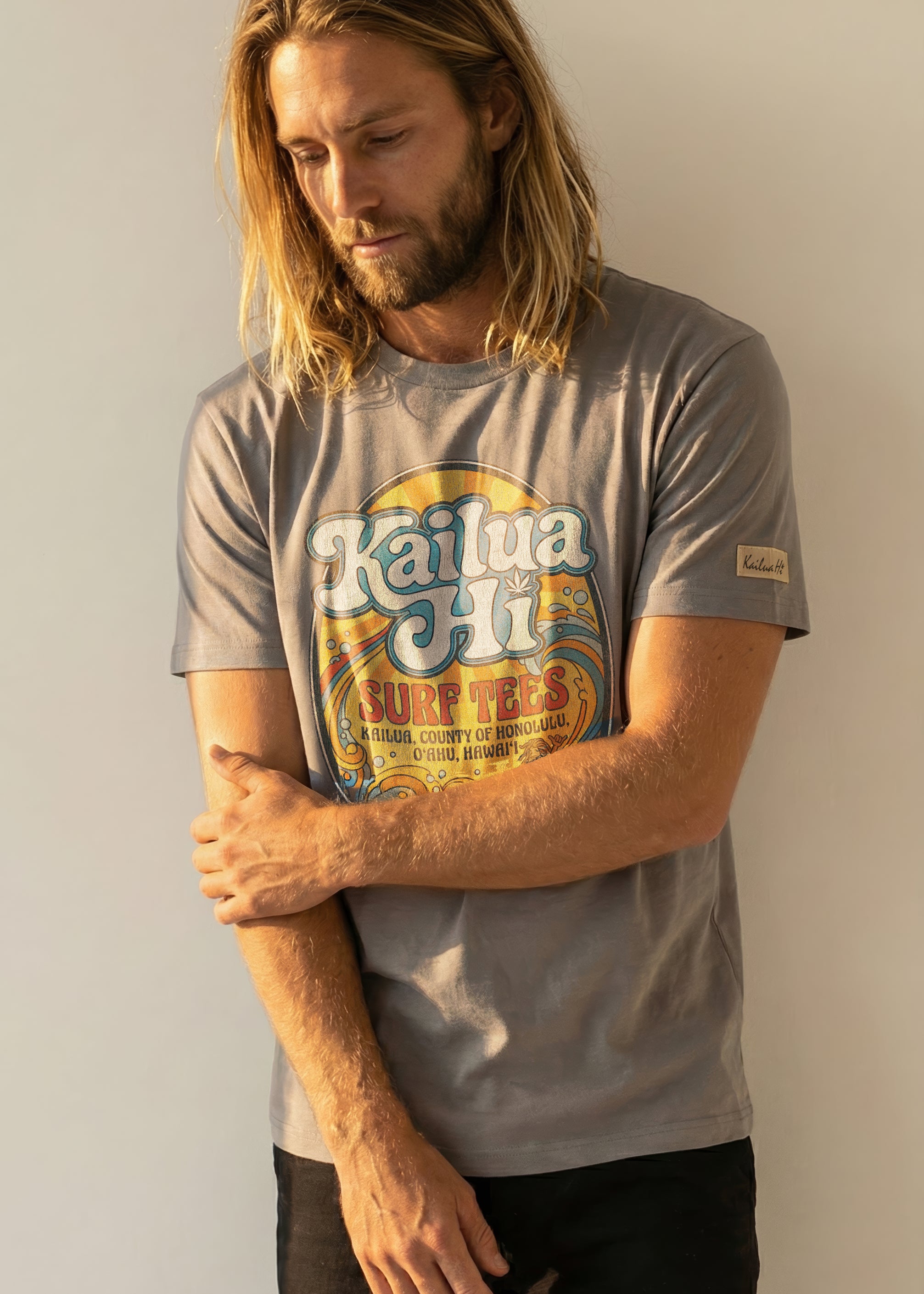 Man wearing a gray t-shirt with a kailua hi logo graphic design on a plain background