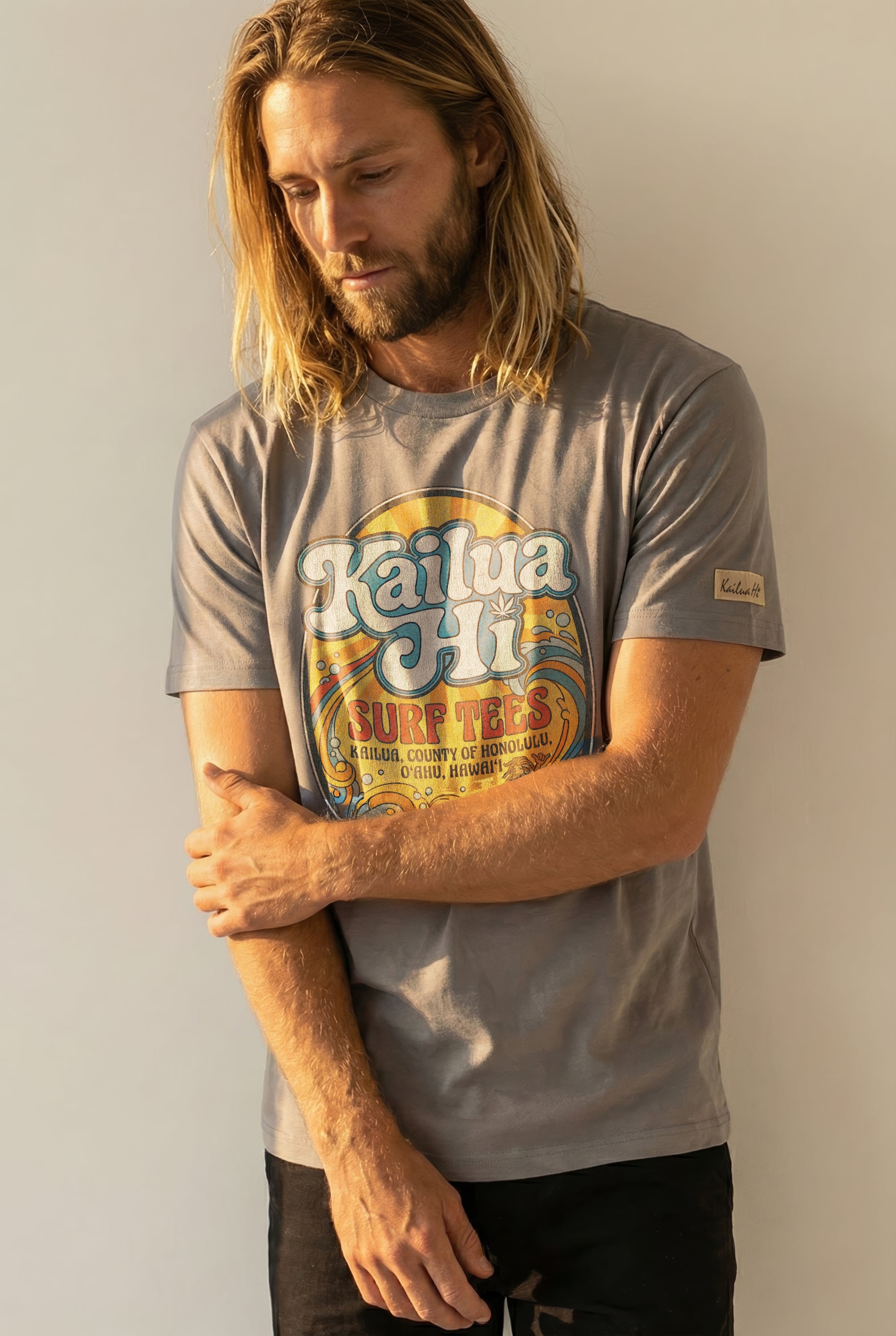 Man wearing a gray t-shirt with a kailua hi logo graphic design on a plain background