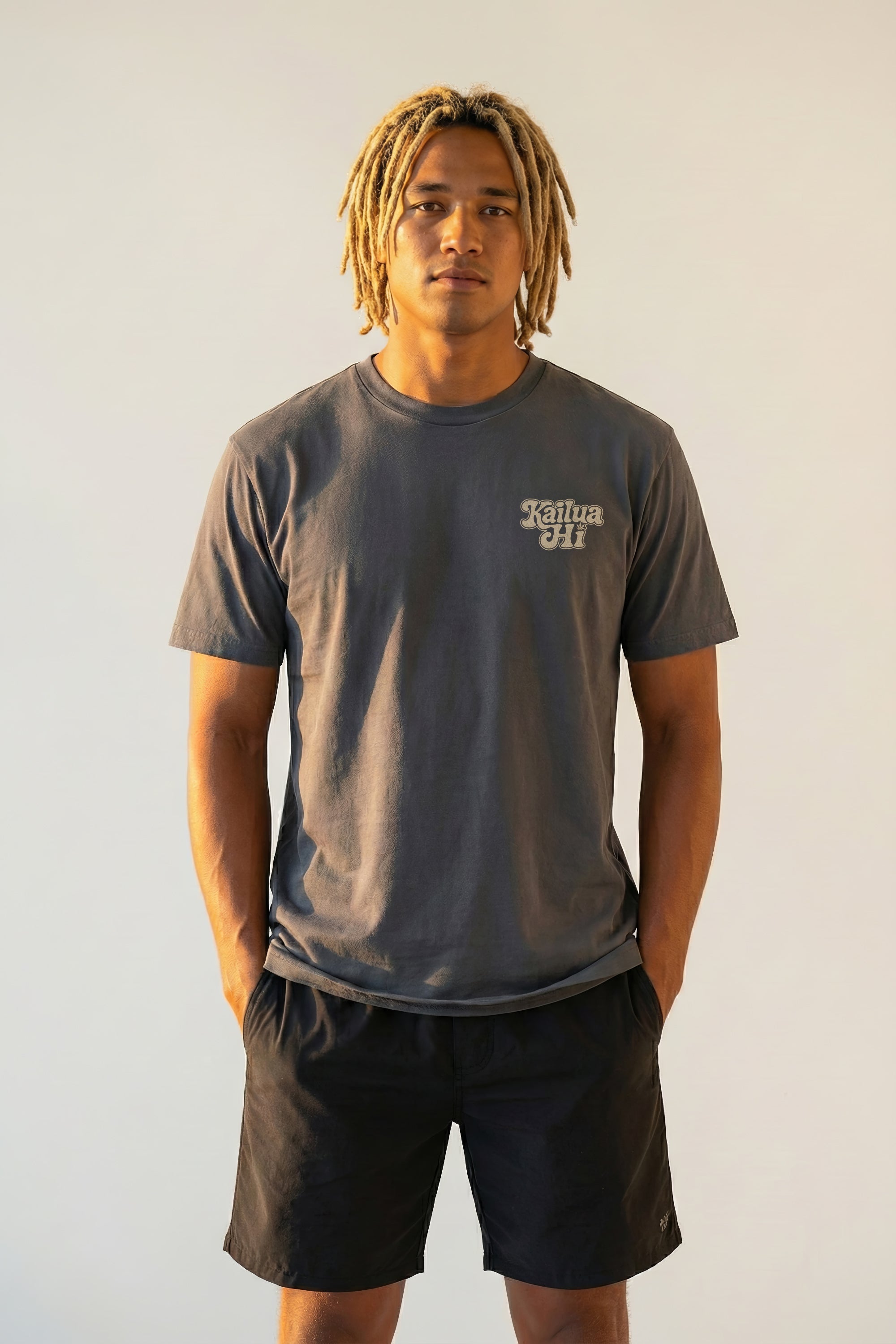Man wearing a dark gray kailua hi vintage tee logo shirt and black shorts against a plain background