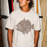 a man wearing a pearl colored t-shirt with a fish graphic standing in front of some surfboards