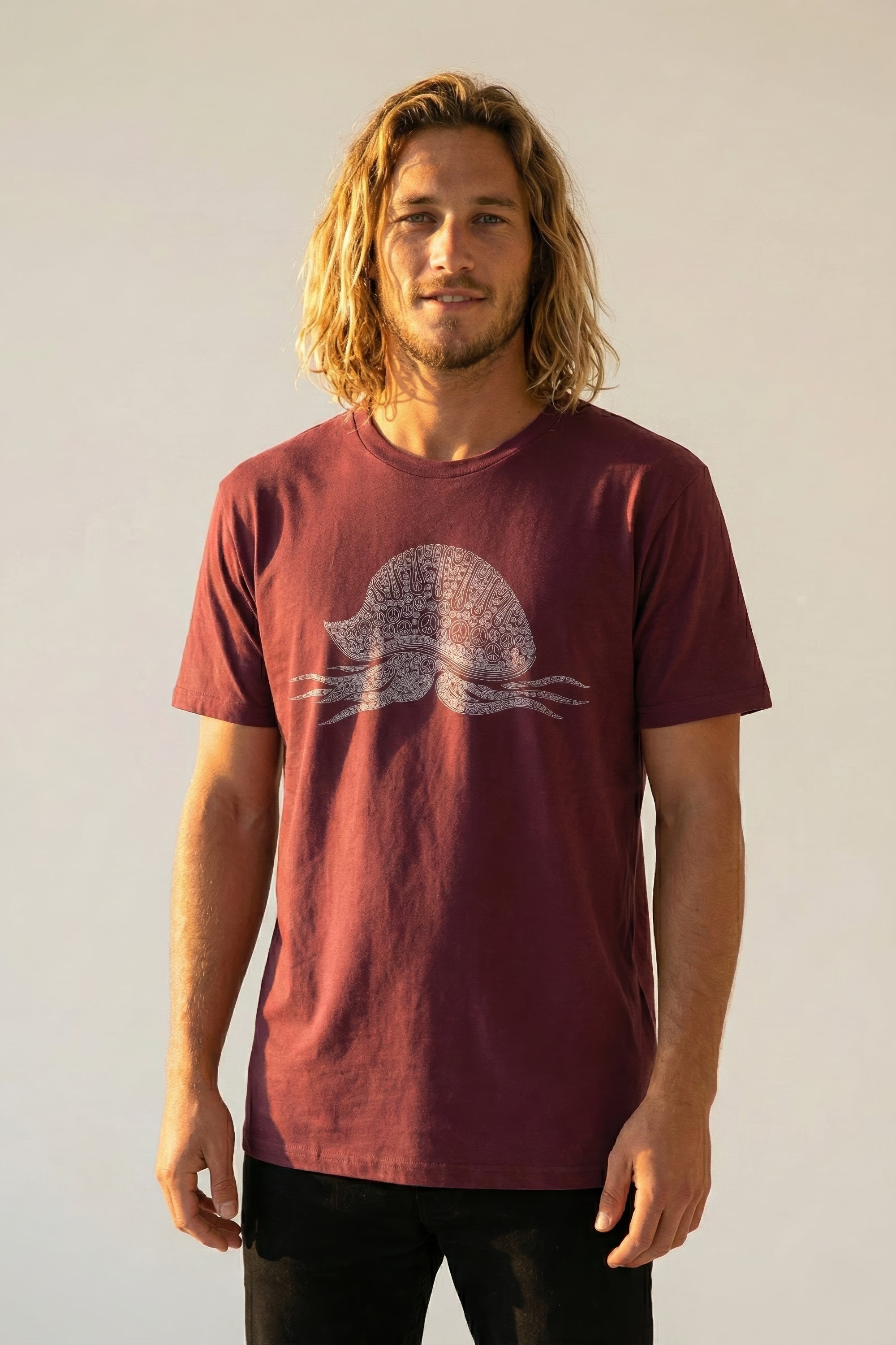 Man wearing a burgundy t-shirt with a white man-o-war with peace signs graphic design on a plain background