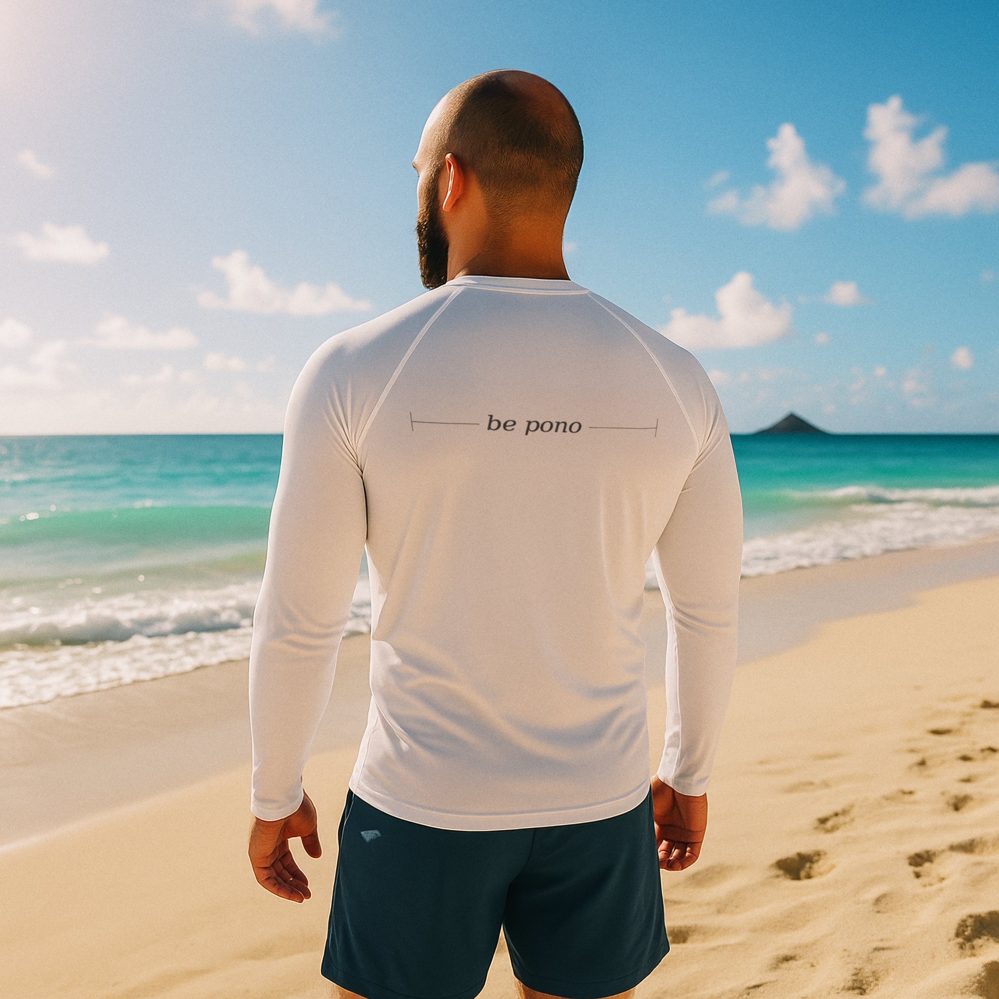 man in white long-sleeve rash guard with “be pono” back print walking along the Kailua shoreline