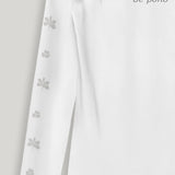 White fabric with a flower pattern on the sleeves on a light gray background, featuring the grey text 'be pono'.