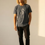 man wearing a grayish blue t-shirt with a seahorse design against a plain background