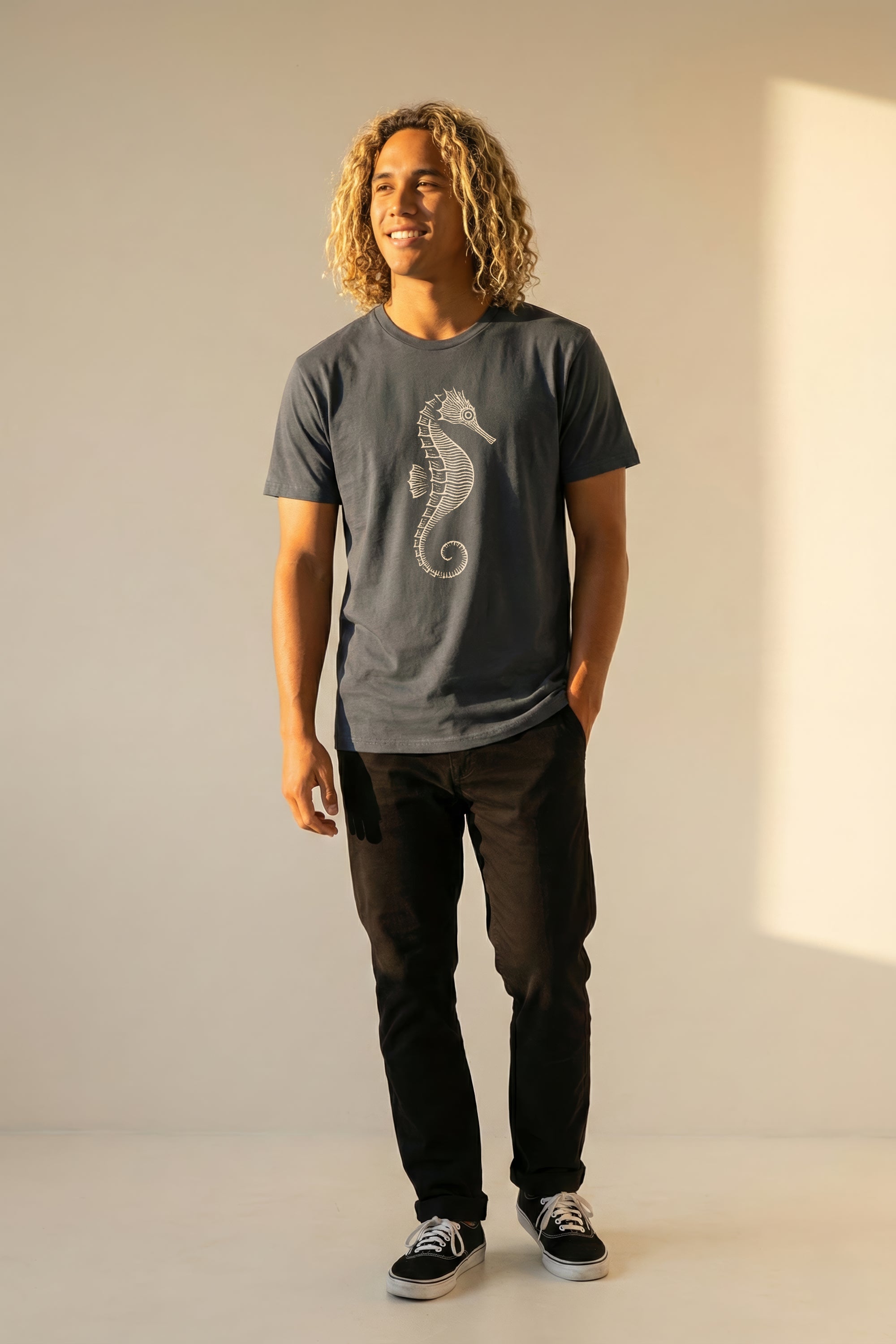 man wearing a grayish blue t-shirt with a seahorse design against a plain background