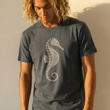 man wearing a grayish blue t-shirt with a seahorse design against a plain background