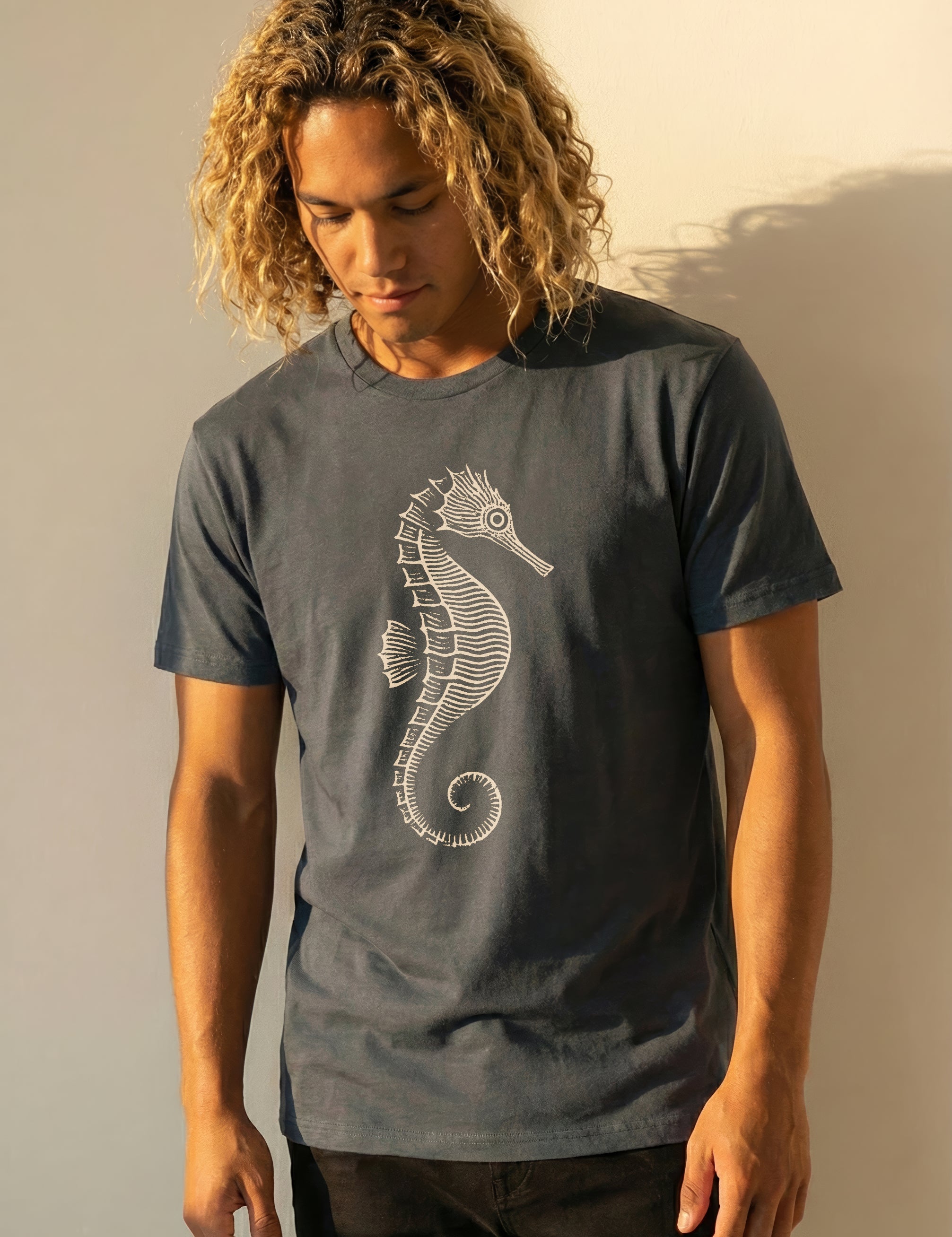 man wearing a grayish blue t-shirt with a seahorse design against a plain background