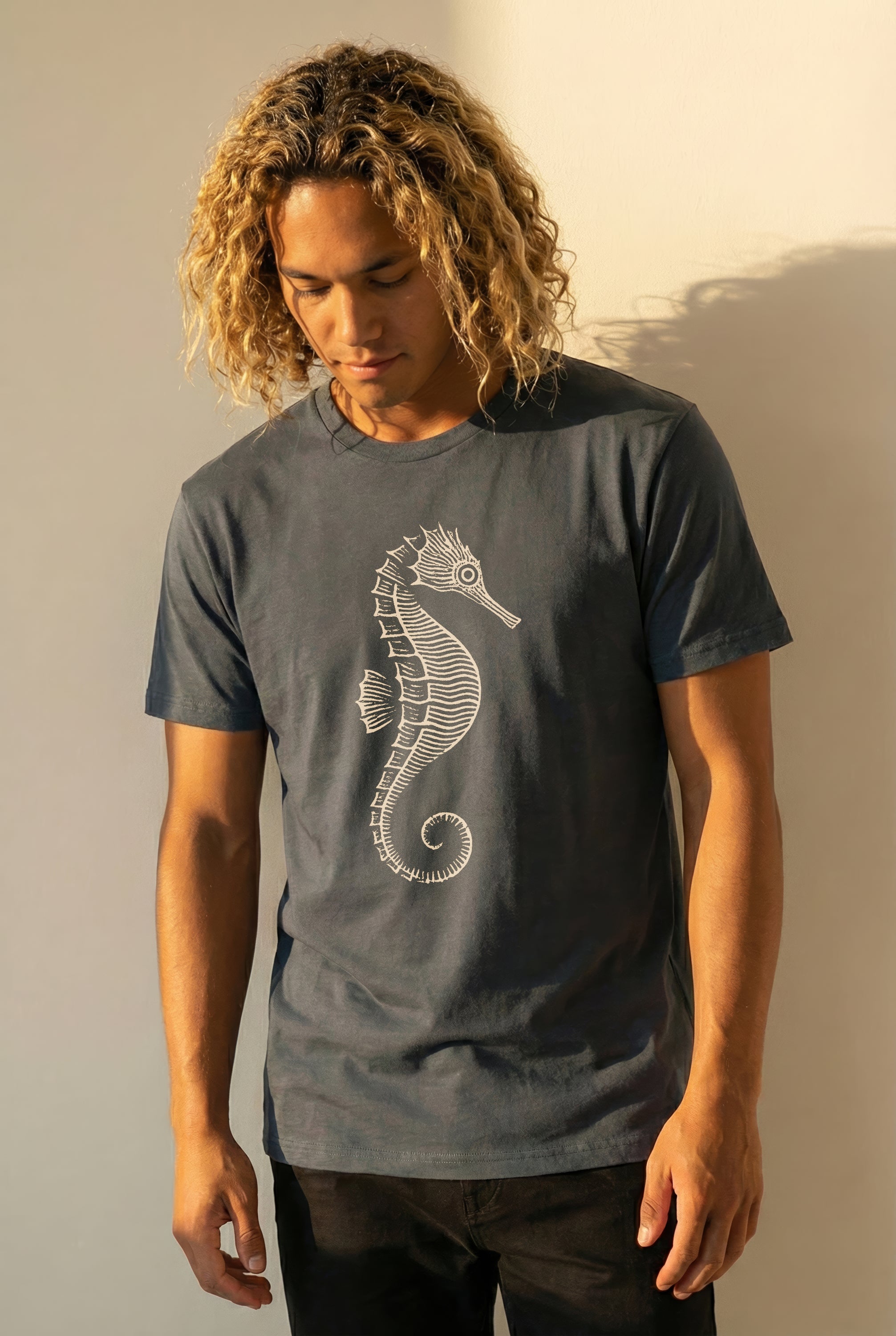 man wearing a grayish blue t-shirt with a seahorse design against a plain background