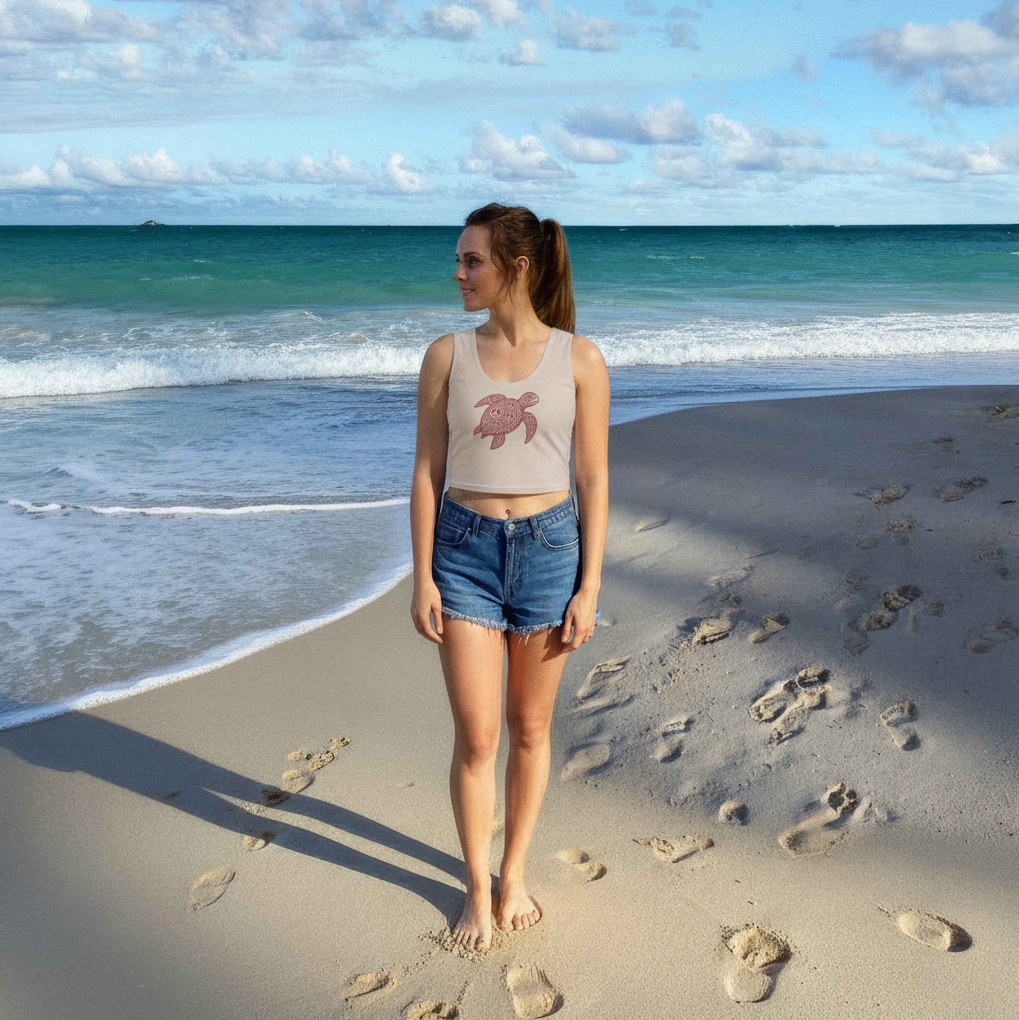 woman on Kailua beach wearing a light-rose crop top with a burgundy honu (sea turtle) graphic, looking toward the ocean