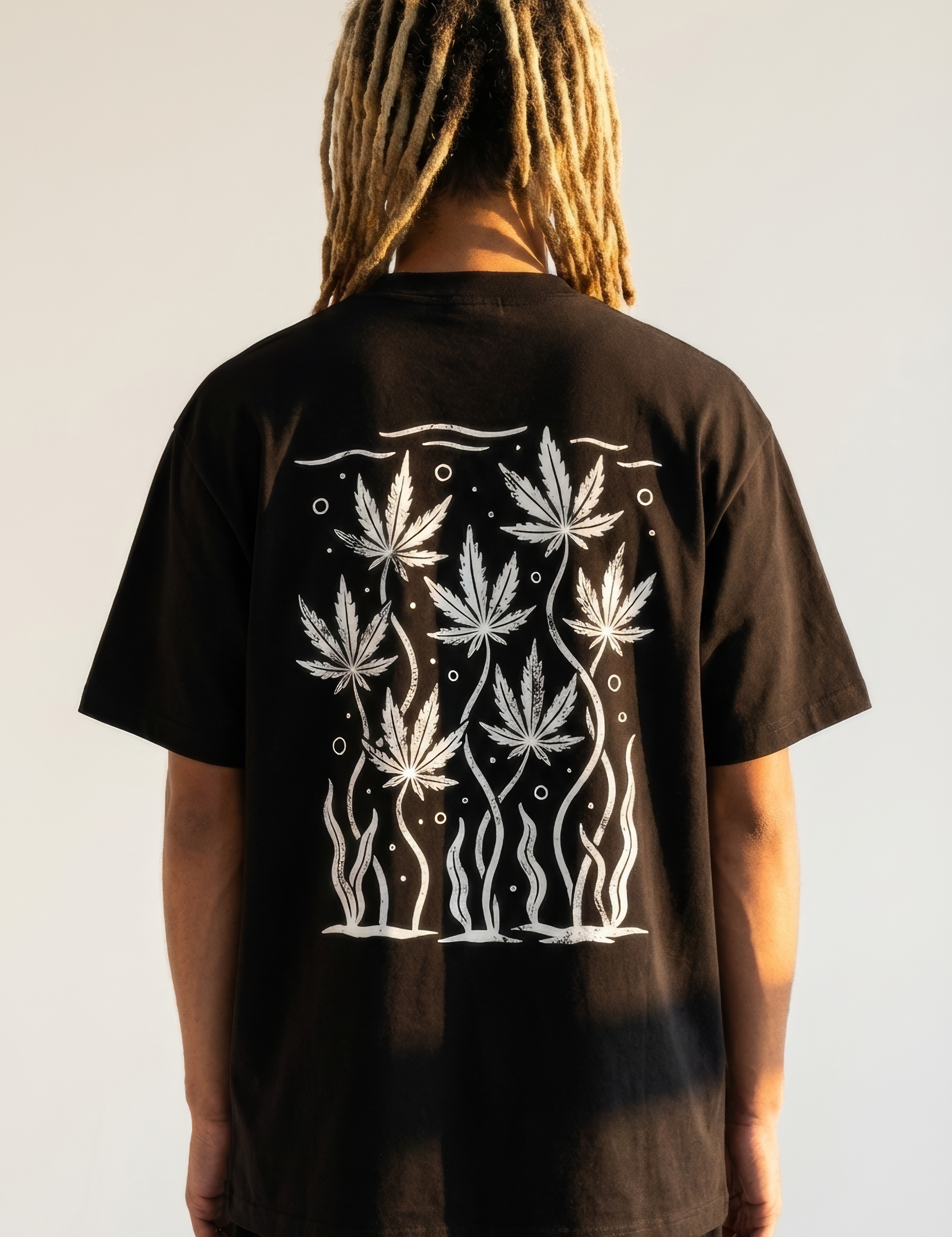 Person wearing a black t-shirt with white cannabis leaf design on the back against a plain background