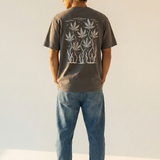 Person wearing a dark gray t-shirt with a white cannabis leaf graphic design on the back, standing against a plain background.