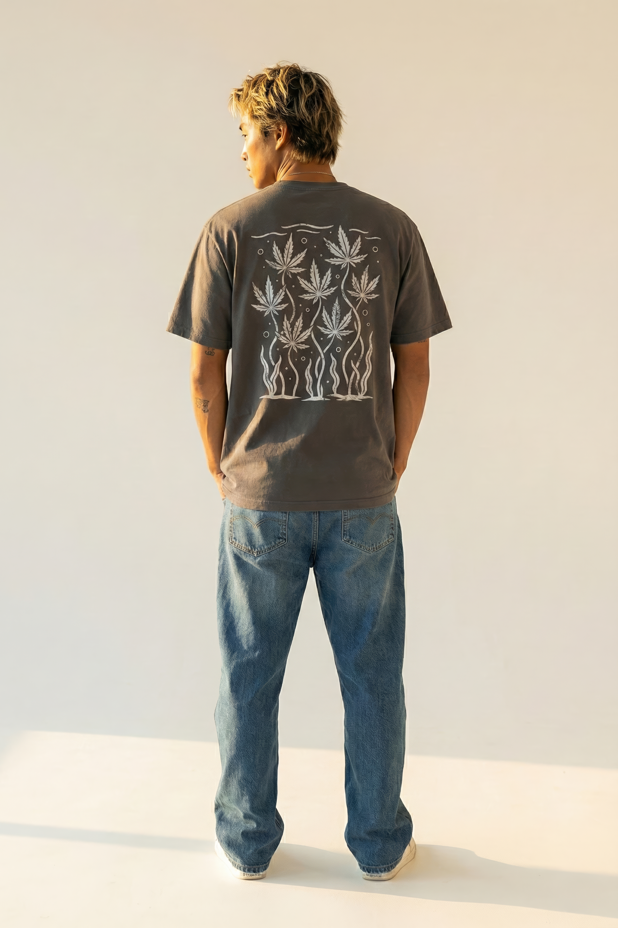 Person wearing a dark gray t-shirt with a white cannabis leaf graphic design on the back, standing against a plain background.