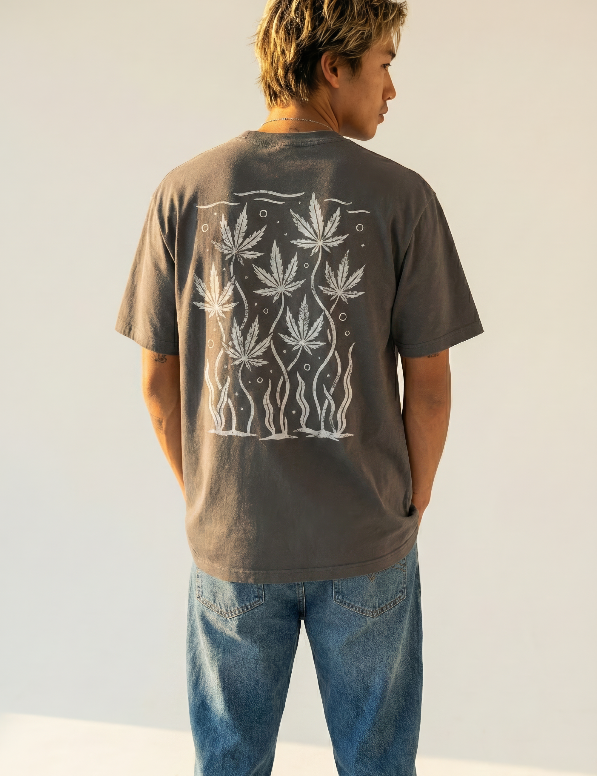 Person wearing a dark gray t-shirt with white cannabis leaf design on the back, standing against a plain background.