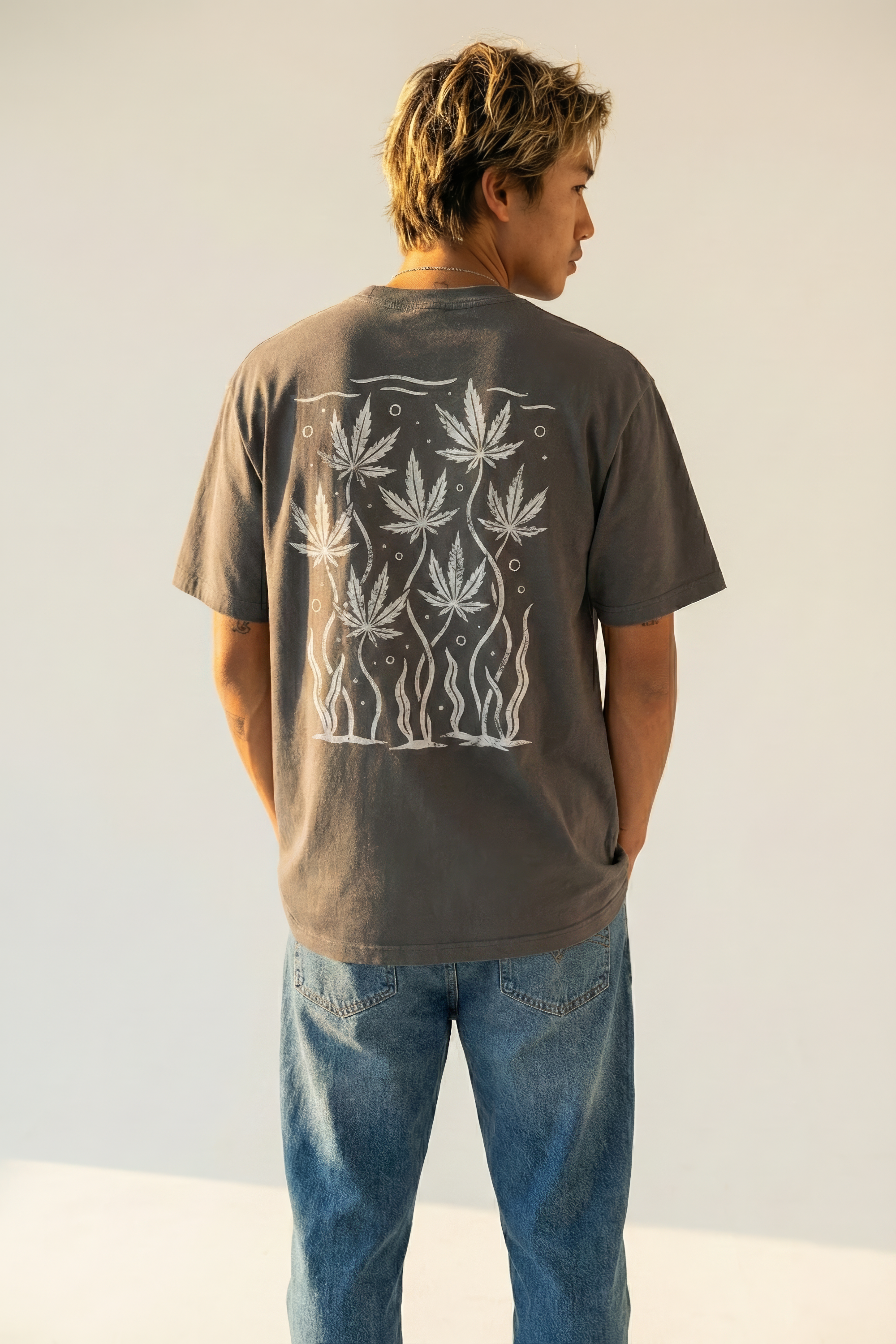 Person wearing a dark gray t-shirt with white cannabis leaf design on the back, standing against a plain background.