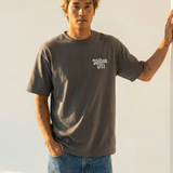 Man wearing a gray t-shirt with a white kailua hi logo and blue jeans against a light background