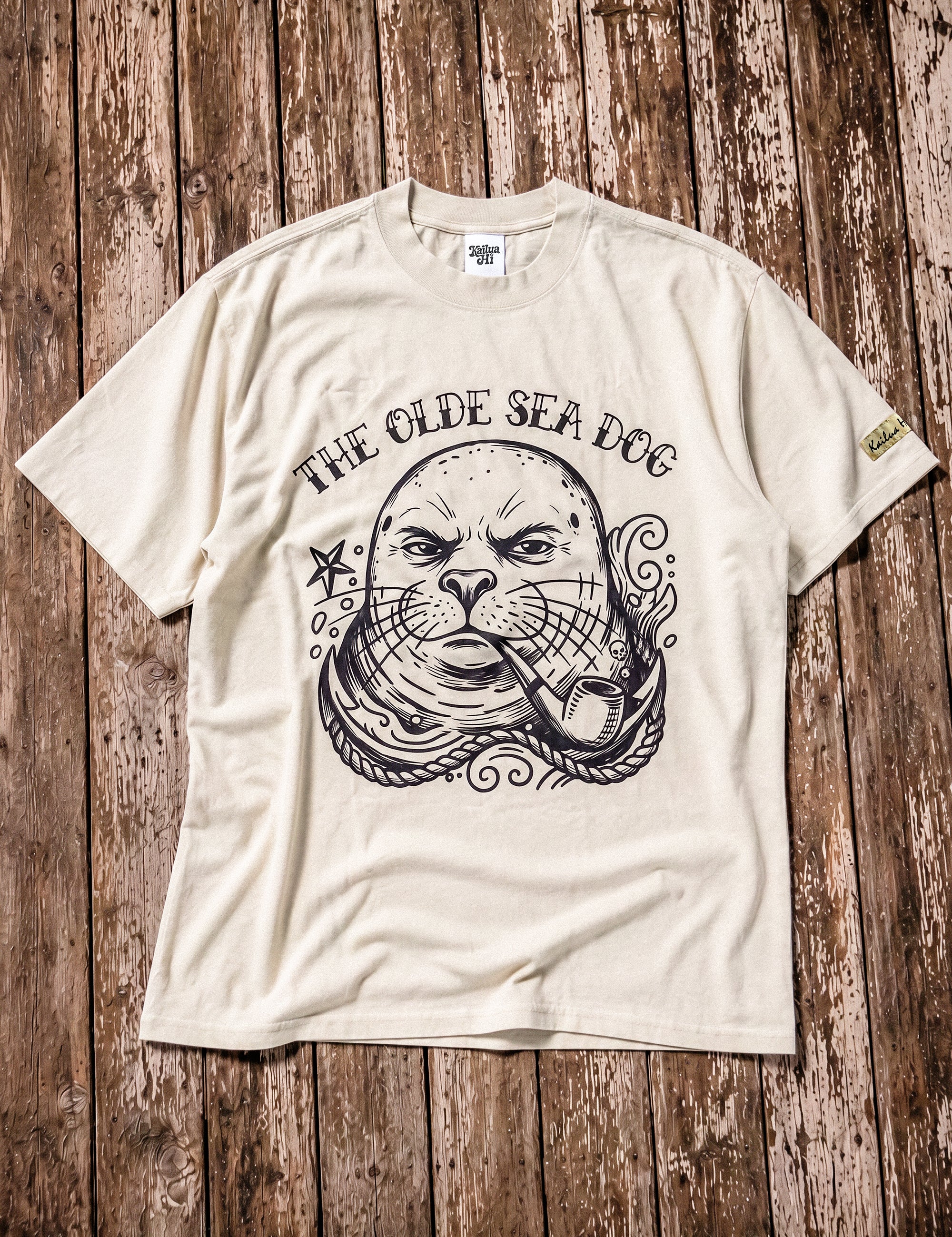 a faded green graphic tee with a monk seal design laying on a wood floor